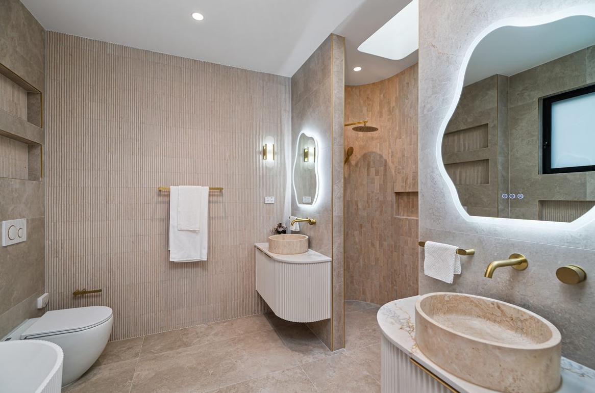 Wavy mirror above a stone vanity with travertine tiling